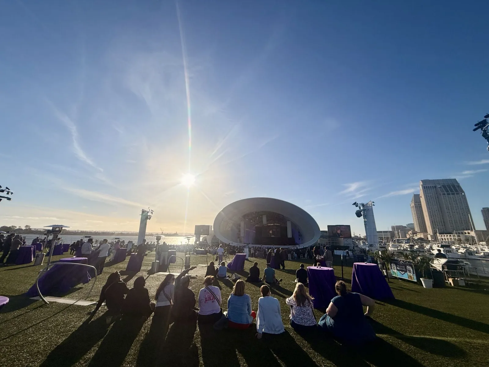 Sunset over the open-air main stage on the San Diego waterfront, attendees seated on the grass.
