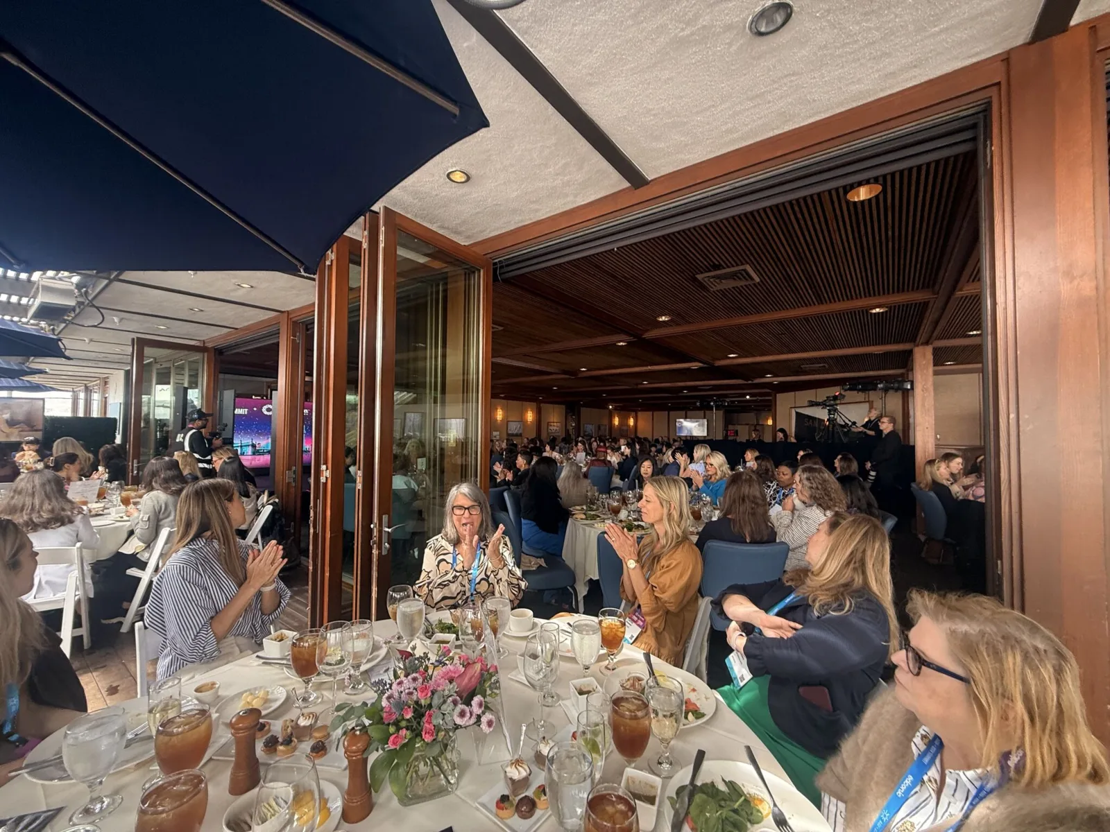 Conference dinner with attendees applauding around tables, warm interior light.